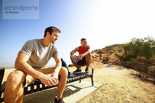 Zwei männliche Freunde  sitzend auf der Bank  auf der Klippe  mit Blick auf die Aussicht.