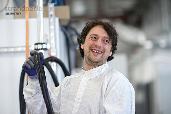Mittlerer erwachsener Mann im Laborkittel mit Industrie-Rohrleitung  lächelnd wegblickend