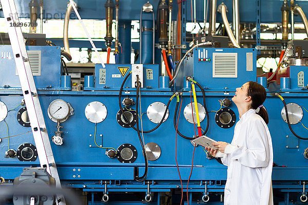 Junge Frau im Laborkittel mit digitalem Tablett  Blick auf wissenschaftliche Geräte lächelnd