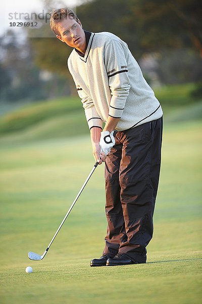 Golfer hält Golfschläger  der sich darauf vorbereitet  Goldschwung zu nehmen  und schaut weg.