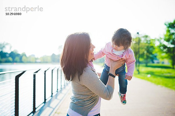Mittlere erwachsene Frau hebt Kleinkind-Tochter am Flussufer auf