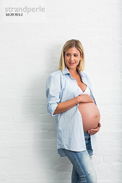 Vollzeitschwangerschaft junge Frau  die sich an die Wand lehnt und den Bauch hält