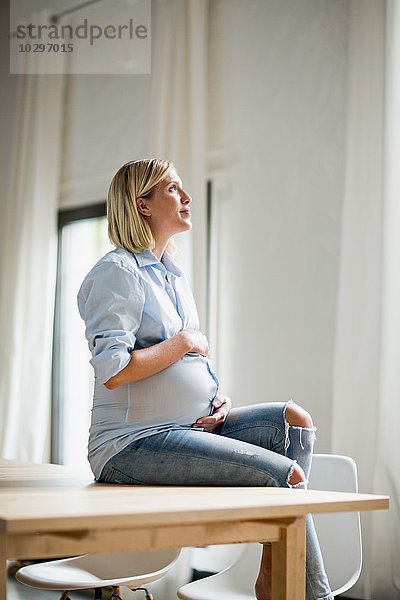 Vollzeitschwangerschaft junge Frau sitzt auf dem Tisch und hält den Bauch.
