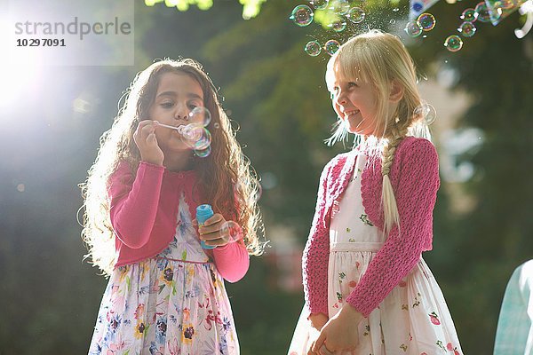 Zwei süße Mädchen blasen Blasen im sonnigen Garten