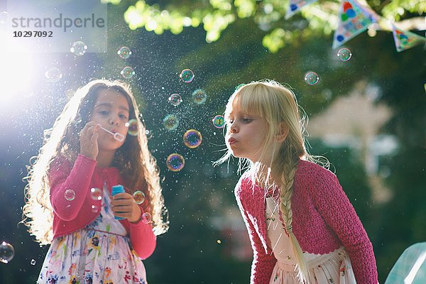 Zwei Mädchen blasen Blasen im sonnigen Garten