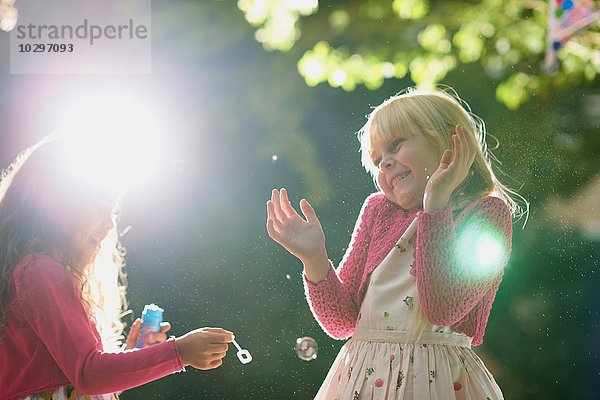 Zwei Mädchen blasen und knallen Blasen im sonnigen Garten.
