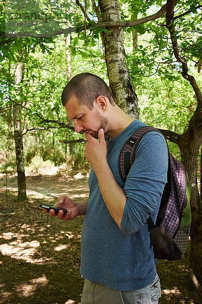 Männlicher Wanderer mit Blick auf das Smartphone im Wald