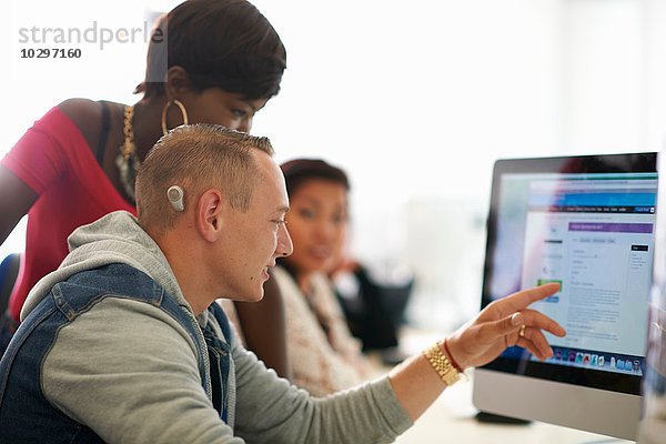 Gruppe von Schülern  die auf Desktop-Computer im Klassenzimmer zeigen