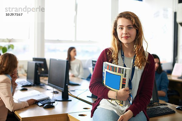 Porträt einer Studentin  die eine Datei vor der Computerklasse hält