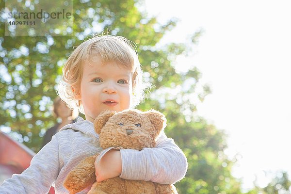 Porträt eines niedlichen weiblichen Kleinkindes mit Teddybär auf der Spielplatzrutsche