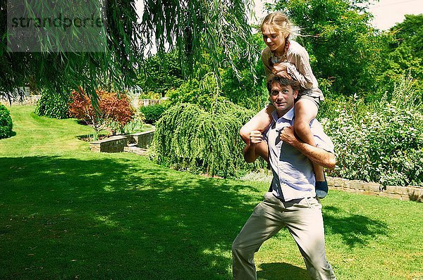 Erwachsener Mann mit Tochter auf den Schultern im Garten