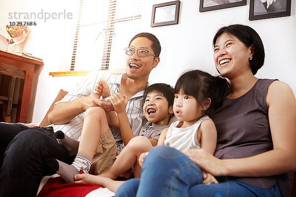 Junge  moderne chinesische Familie von Eltern und zwei kleinen Kindern  die gemeinsam zu Hause auf dem Sofa sitzen und fernsehen.