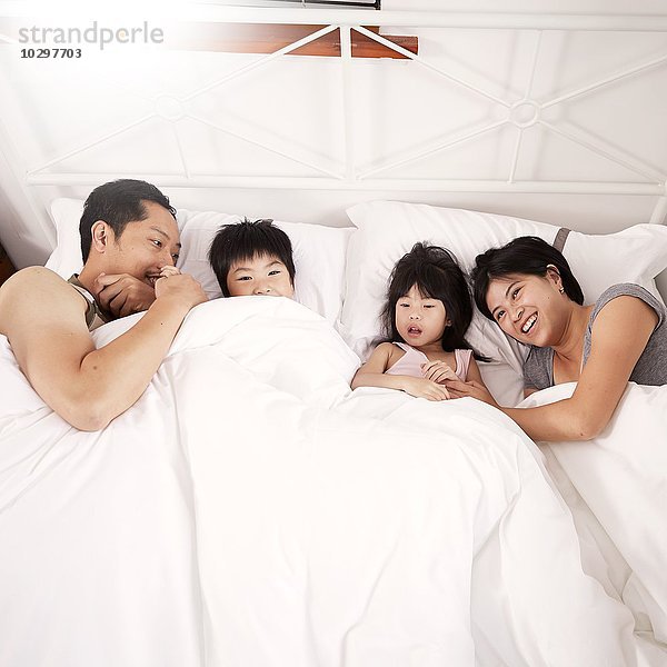 Junge chinesische Elternfamilie und zwei kleine Kinder  die zu Hause zusammen im Bett liegen