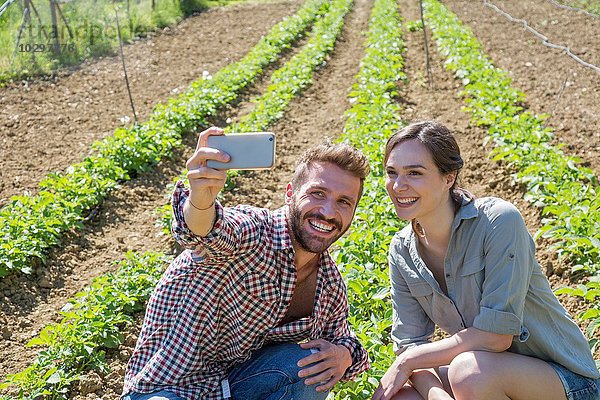 Junges Paar im Gemüsegarten geduckt mit dem Smartphone  um Selfie zu nehmen.