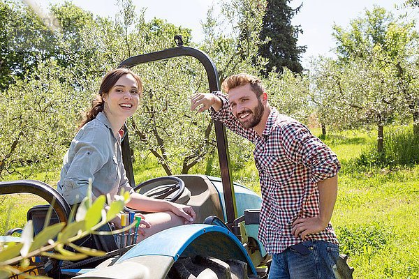 Junges Paar mit Traktor sieht lächelnd in die Kamera