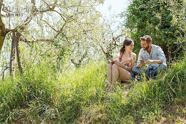 Niedriger Blickwinkel auf ein junges Paar  das auf einem Hügel sitzt und ein Smartphone hält.