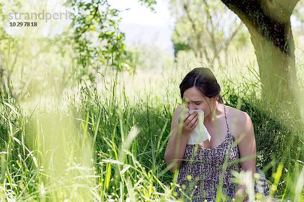 Junge Frau im hohen Gras niesend ins Taschentuch