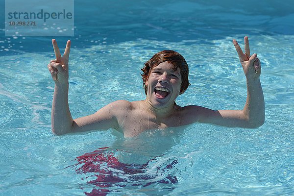 Junge  Teenager im Wasser fröhlich mit Vicoty Zeichen in einem Schwimmbecken