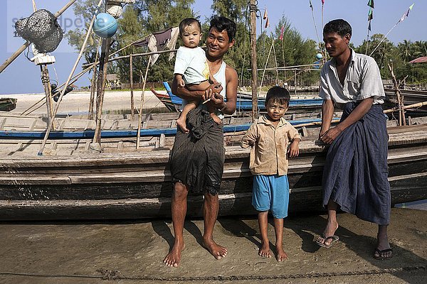 Zwei einheimische Männer und zwei Kinder stehen vor Fischerbooten im Fischerdorf Ngapali  Thandwe  Rakhine-Staat  Myanmar  Asien