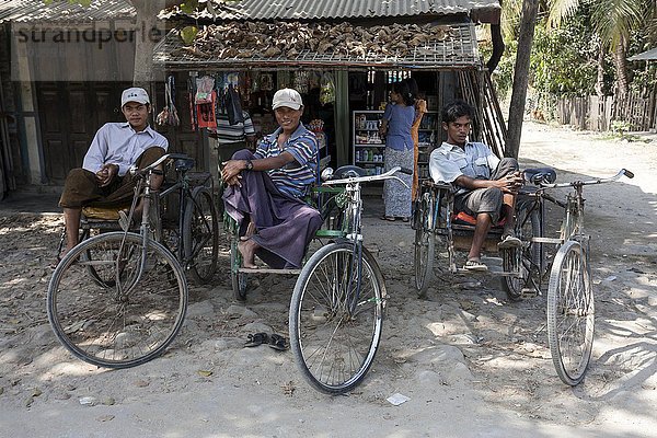 Einheimische Rikscha-Fahrer sitzen auf ihren Rikschas und warten auf Kundschaft  hinten ein kleiner Laden  Ngapali  Thandwe  Rakhine-Staat  Myanmar  Asien