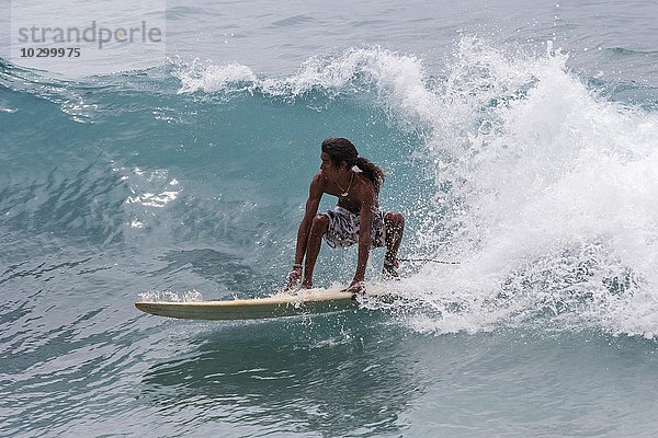 Einheimischer junger Mann reitet mit dem Surfbrett auf den Wellen  Wellenreiter  Anse Patates  Indischer Ozean  Insel La Digue  Seychellen  Afrika