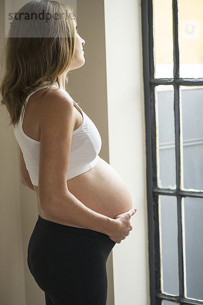 Schwangere Frau schaut nachdenklich aus dem Fenster