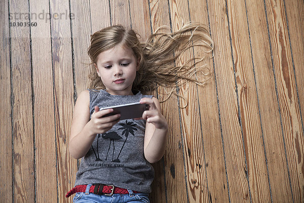 Kleines Mädchen auf dem Boden liegend mit Smartphone