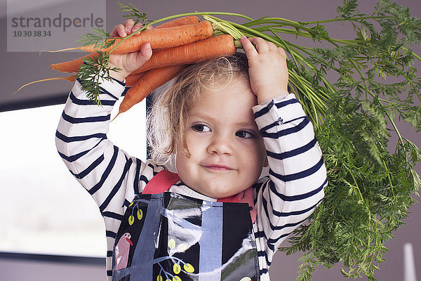 Kleines Mädchen hält frische Karotten über den Kopf  Portrait