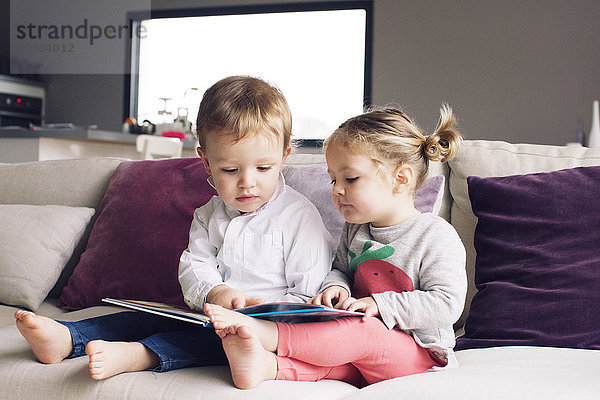 Junge Geschwister beim gemeinsamen Betrachten des Buches auf dem Sofa