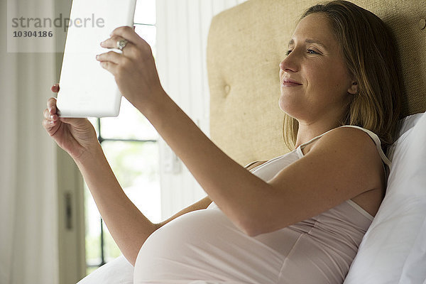 Schwangere Frau mit digitalem Tablett zum Video-Chat mit Freunden und Familie
