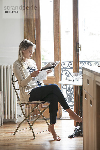Junge Frau beim Zeitungslesen zu Hause