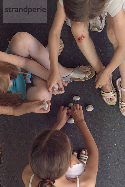 Mädchen sitzen zusammen und spielen mit Kieselsteinen.