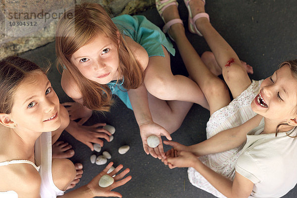 Mädchen sitzen zusammen und spielen mit Kieselsteinen.