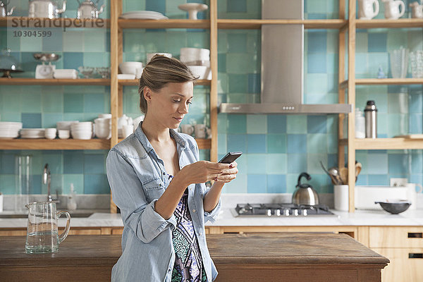 Junge Frau steht in der Küche mit Handy