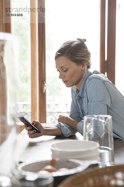 Junge Frau mit Smartphone in der Küche