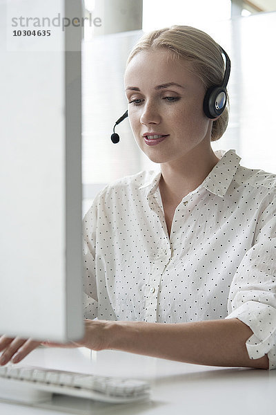 Frau mit Desktop-Computer und Headset im Büro