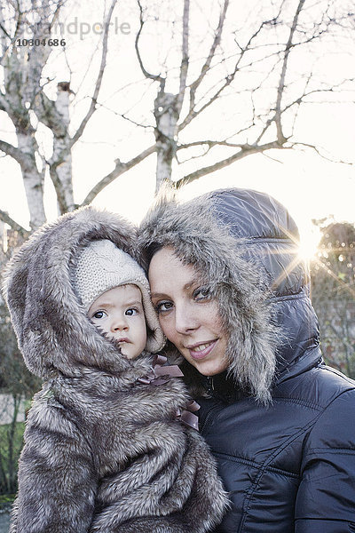Mutter hält Baby im Freien  beide in Wintermänteln  Portrait
