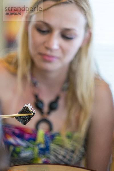 Junge Frau isst Sushi mit Essstäbchen