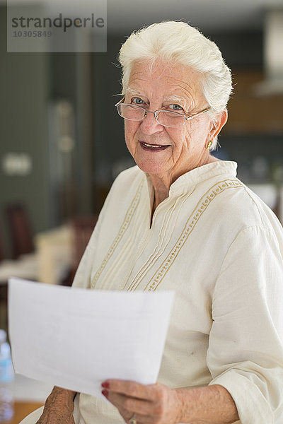 Porträt einer lächelnden Seniorin mit Brille  die ein Blatt Papier hält.