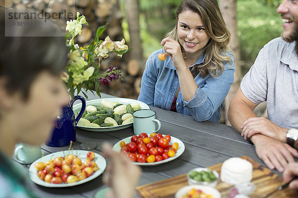 Drei Personen saßen an einem Tisch im Freien  mit frischem Obst und Gemüse in Tellern auf dem Tisch.