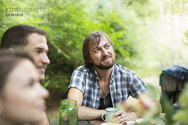 Eine Gruppe von drei Freunden sitzt im Freien um einen Tisch herum und isst zusammen.