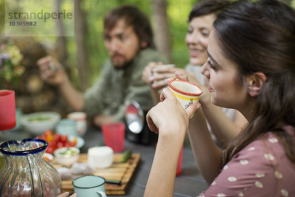 Vier Personen sitzen um einen Holztisch im Wald und teilen sich eine Mahlzeit.