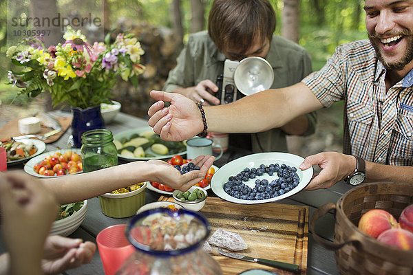 Eine Gruppe von Freunden versammelte sich an einem Tisch im Freien und teilte Gerichte mit frischen Früchten und Salaten.