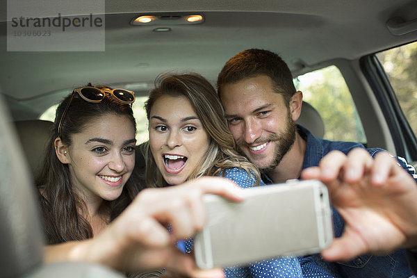 Eine Gruppe von Menschen in einem Auto  zwei Frauen und ein Mann  die ein Selfy nehmen.