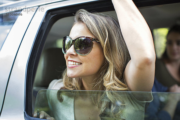 Eine junge Frau lehnt mit erhobenem Arm aus einem Autofenster.