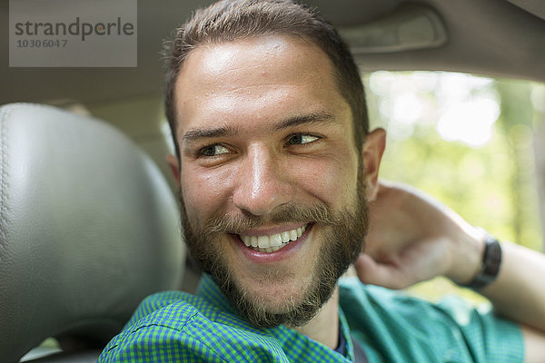 Ein Mann sitzt auf dem Fahrersitz eines Autos und schaut zur Seite.