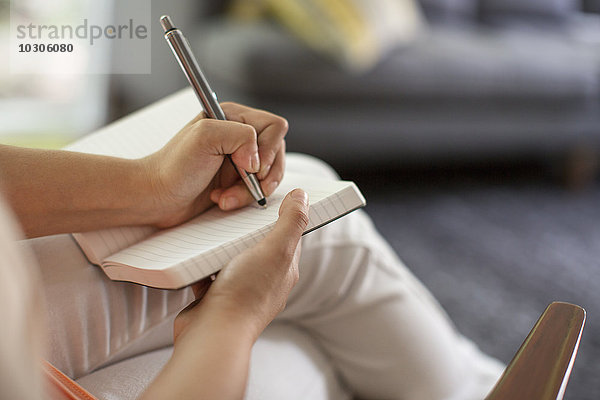 Eine sitzende Frau hält ein offenes Tagebuch und einen Stift in der Hand.