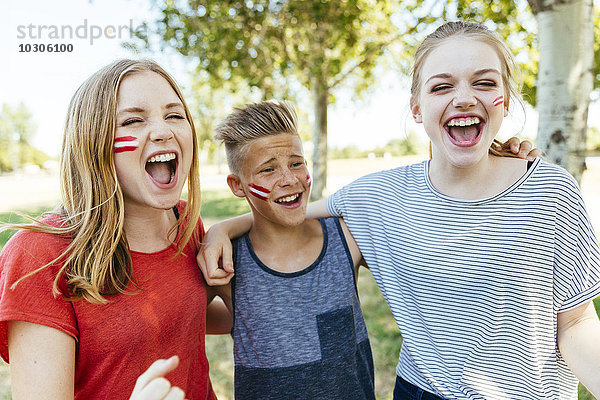 Österreich  drei Teenager mit Nationalfarben auf die Wangen gemalt  die gemeinsam feiern.