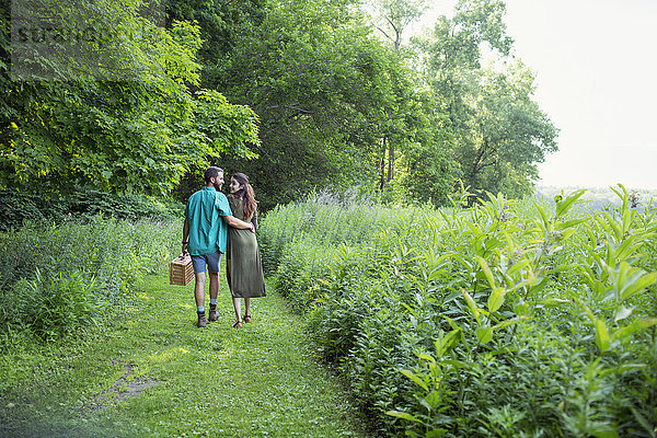 Ein Mann und eine Frau gehen durch eine Wiese  durch das lange Gras und tragen einen Picknickkorb.