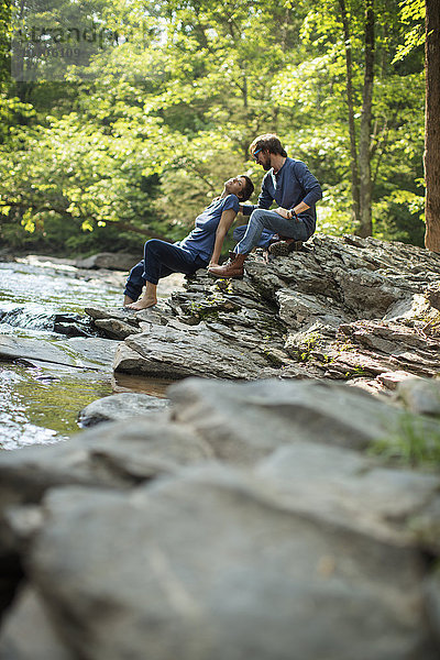Zwei Männer saßen im Schatten auf den Felsen am Fluss.